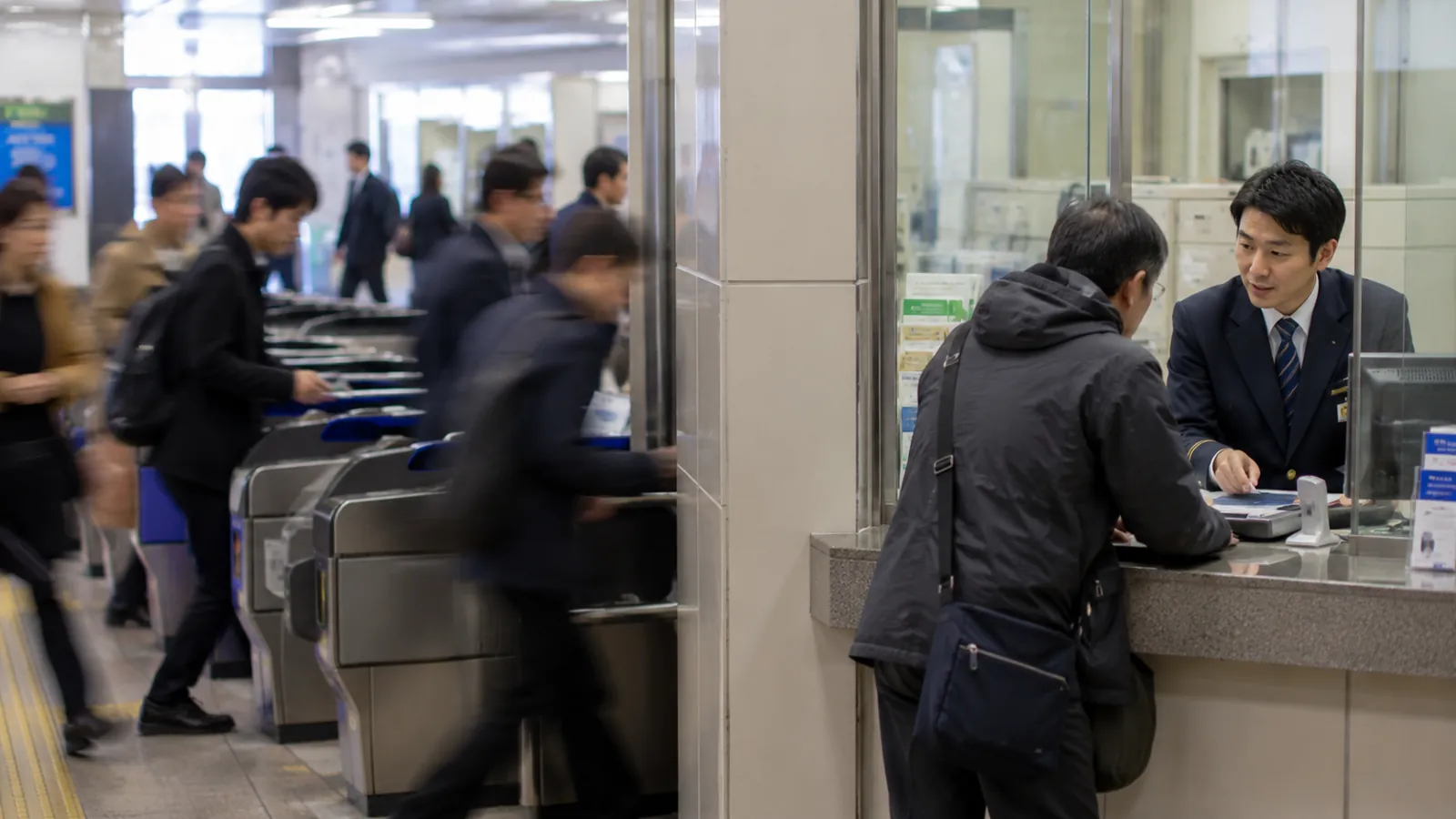 自動改札を素早く通る人々と、窓口でスタッフが丁寧に対応する様子を対比した写真